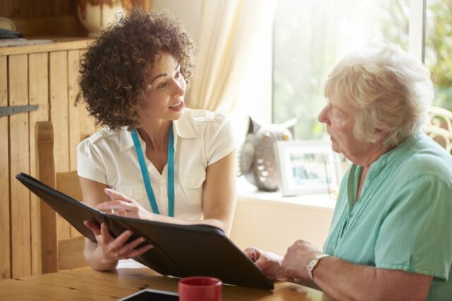 a care worker or medical professional or housing officer makes a house call to a senior client at her home . She is discussing the senior woman’s options on her digital tablet.